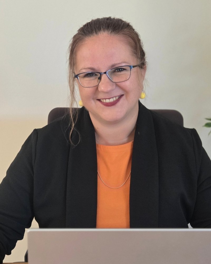 Joanna Laszczak uśmiecha się, siedząc przy biurku z laptopem